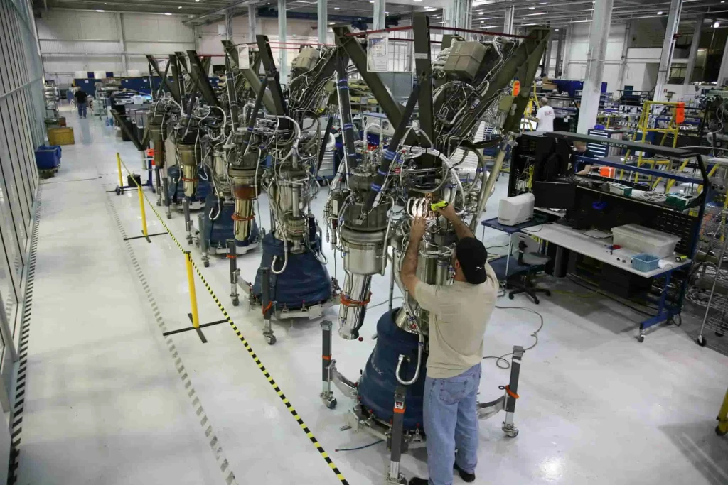 Aerospace manufacturing facility with worker inspecting a row of rocket engines, showcasing precision engineering