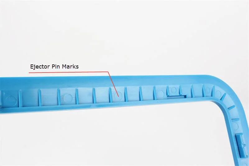 Close up view of a blue plastic part showing ejector pin marks with a labeled arrow pointing to the marks